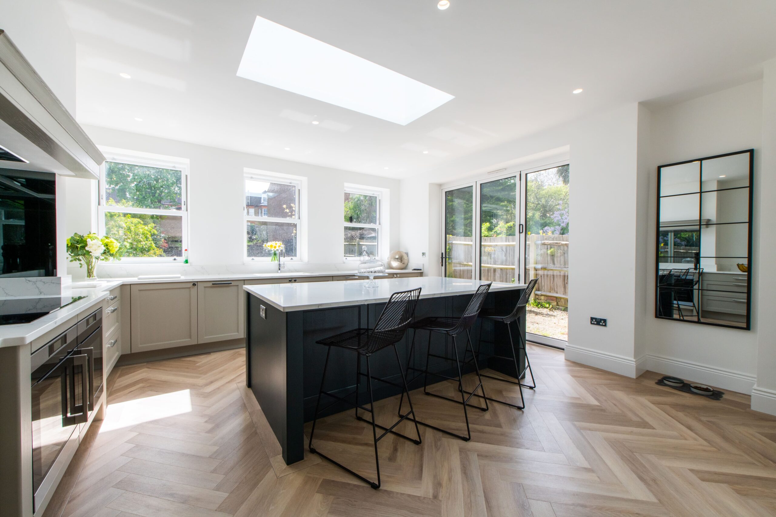 Open plan kitchen with dark island, breakfast bar seating and large garden doors