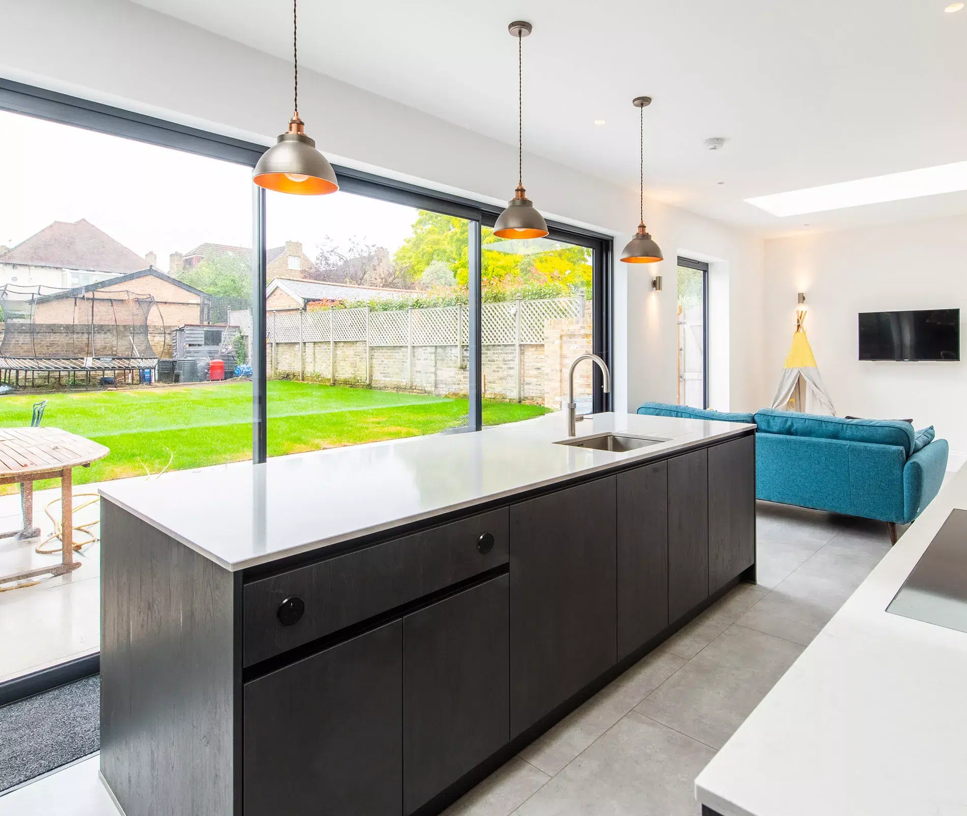 Modern kitchen with dark island, white worktop, pendant lighting and blue sofa in open plan living space