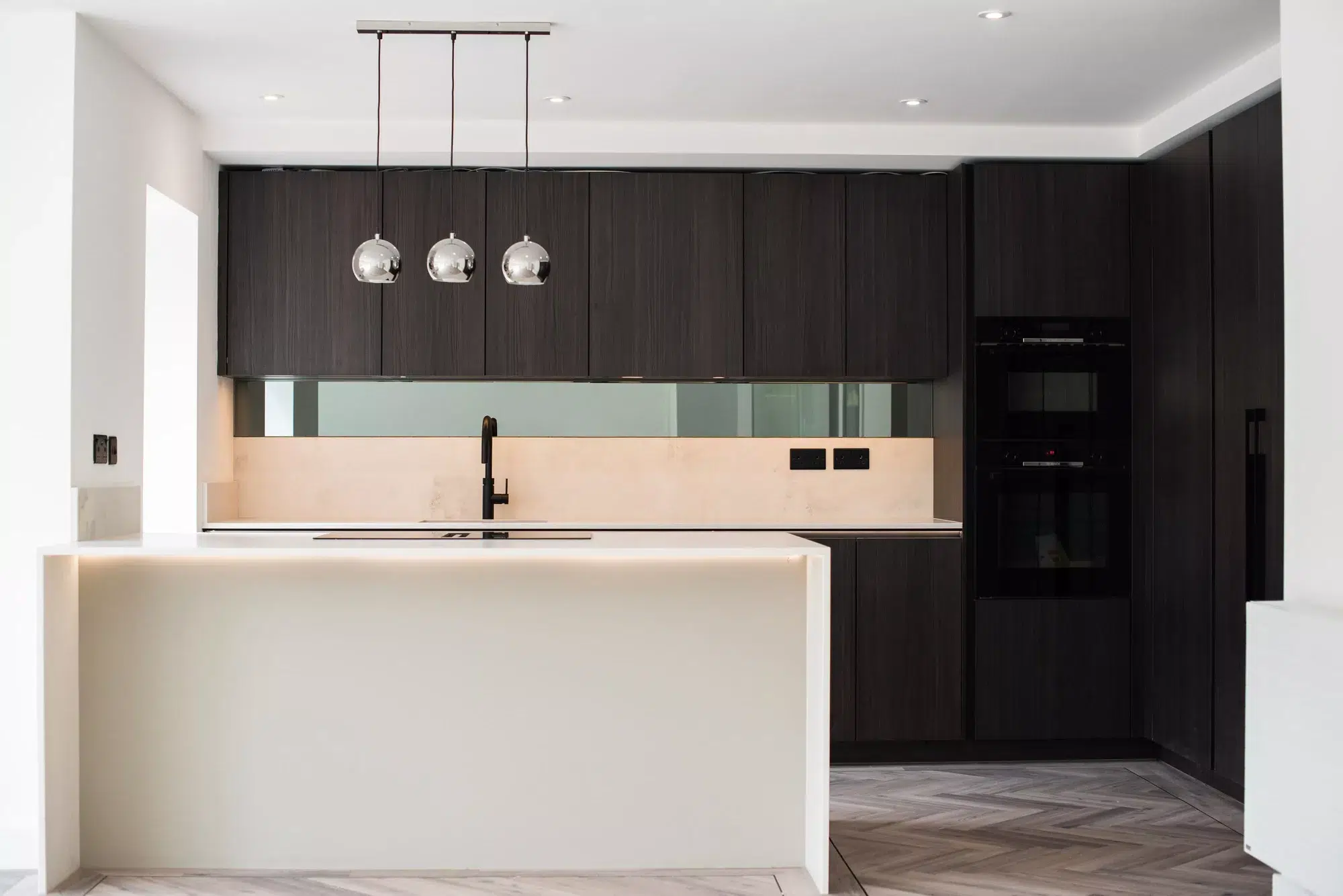 Contemporary family kitchen with illuminated island worktop and dark wood cabinetry by Ornate Kitchens