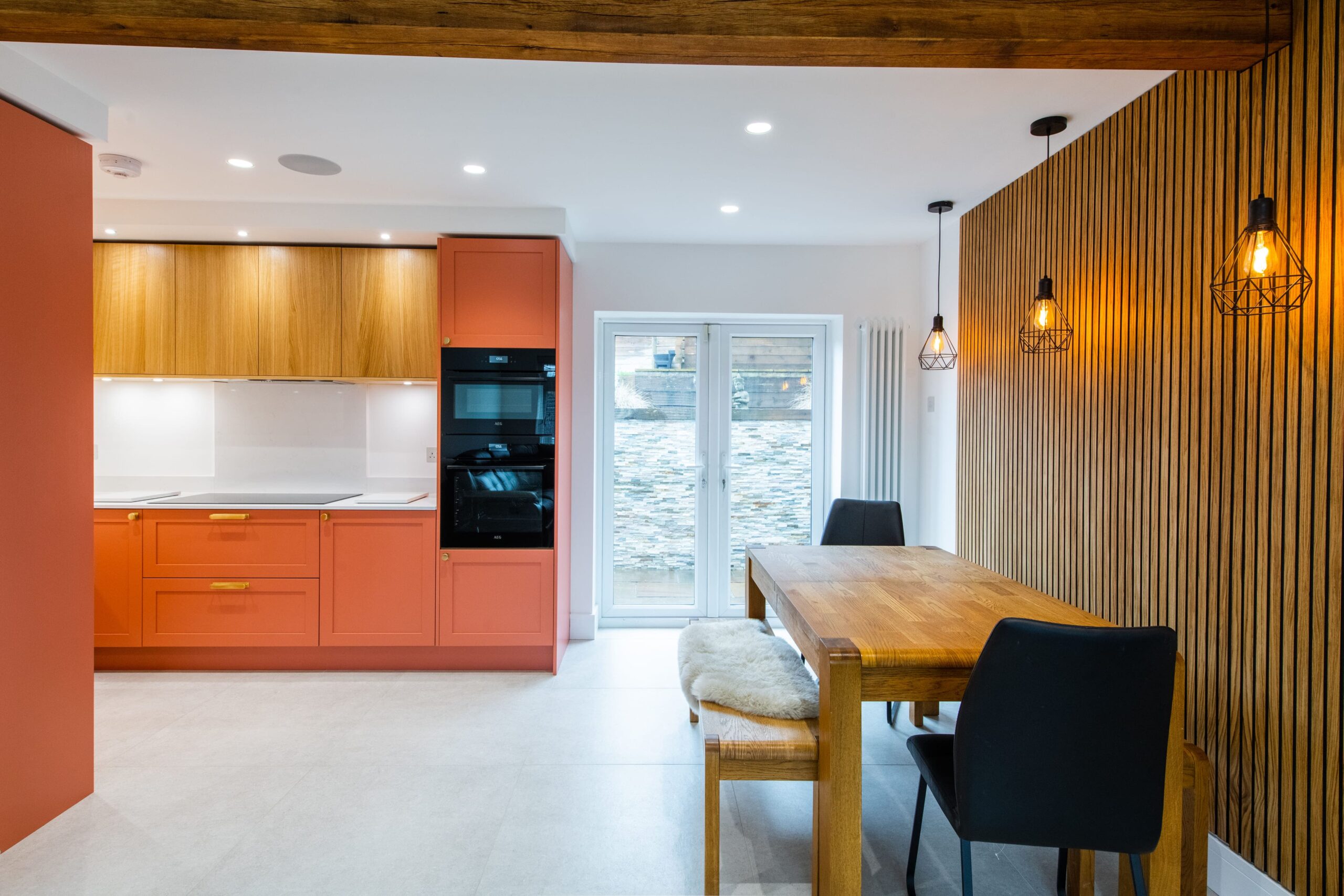 Colourful open plan kitchen diner with coral cabinetry, wooden dining table and feature slatted wall