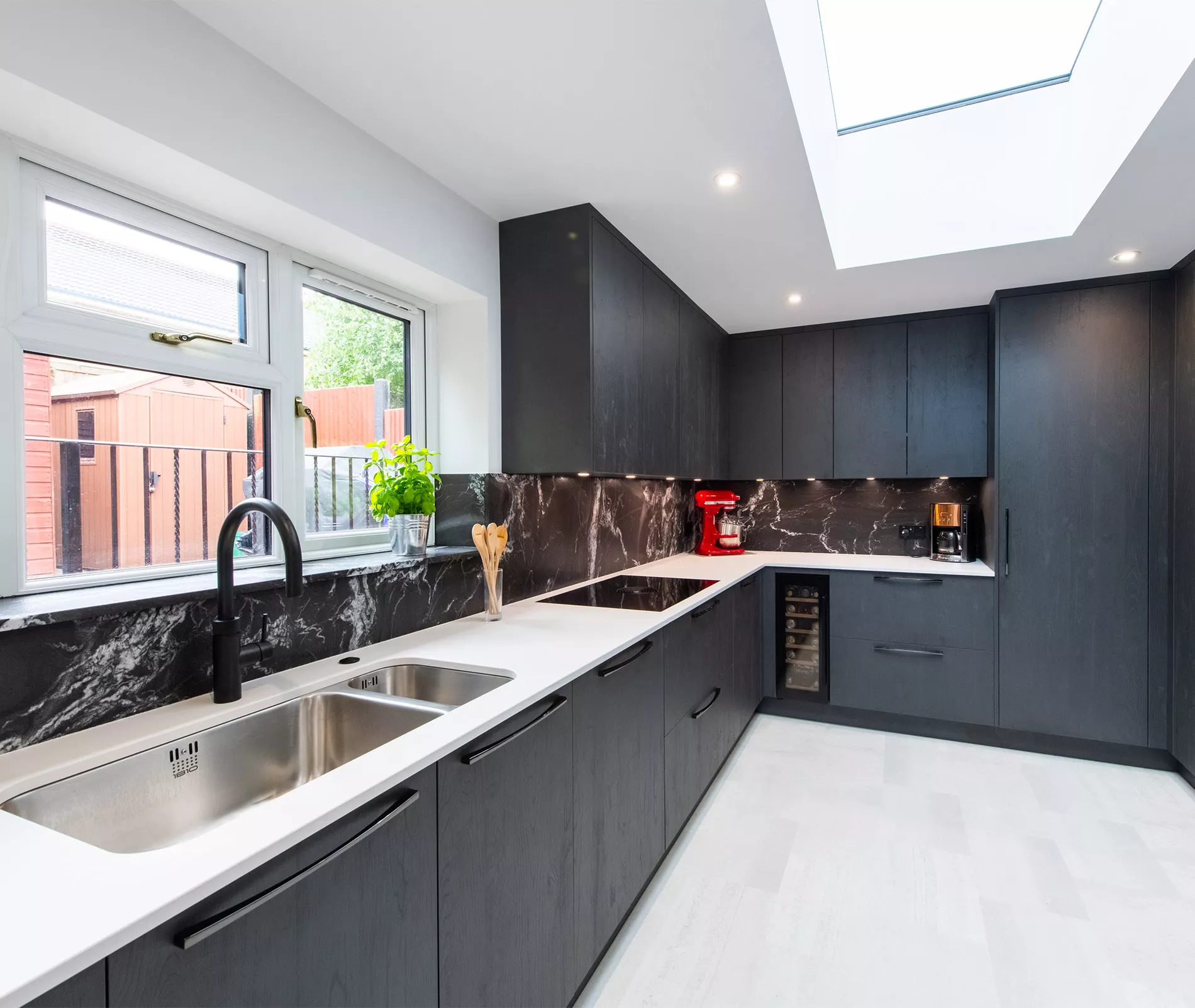 Dark kitchen design with black marble splashback, white worktops and mixed monochrome finishes