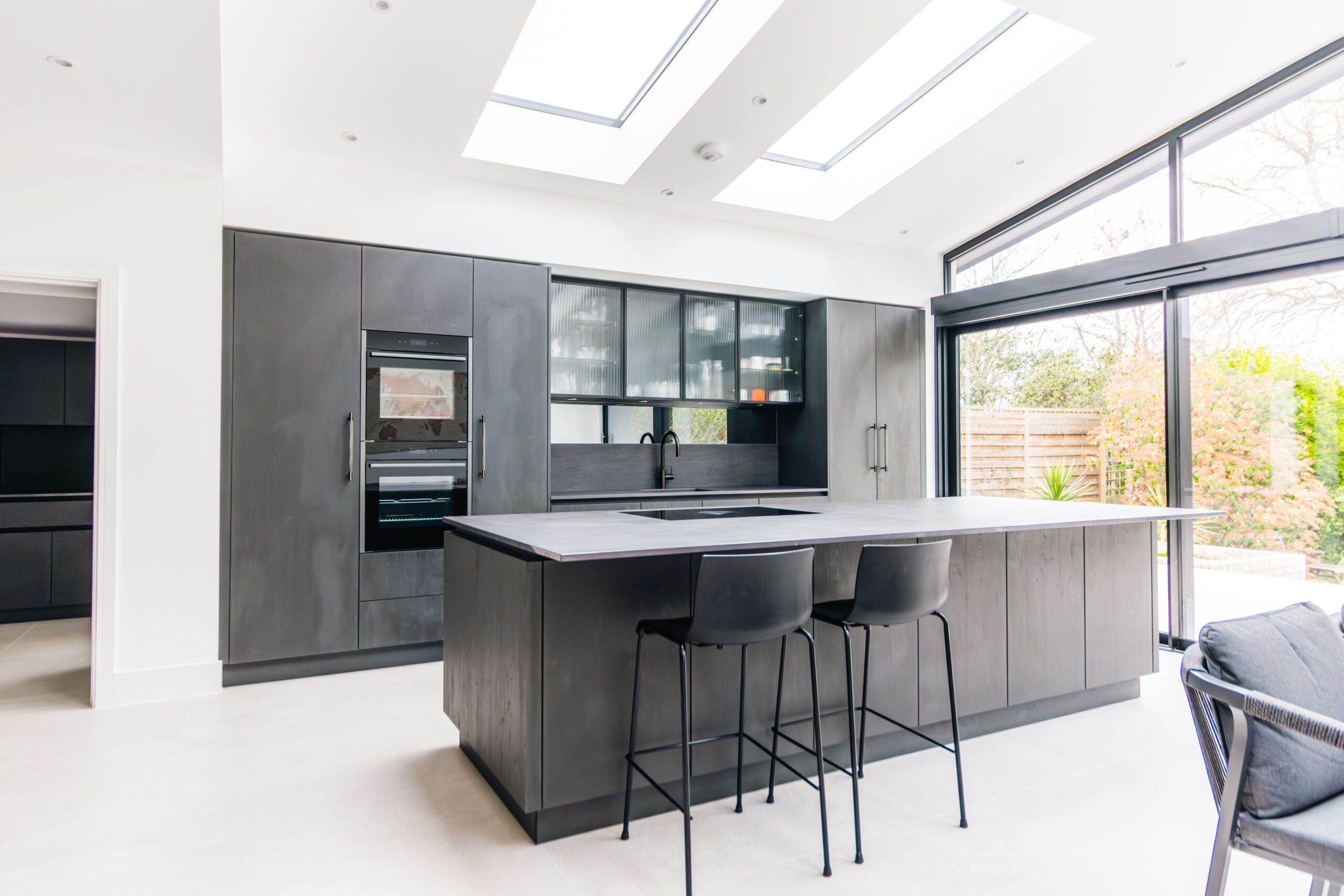 Open plan modern kitchen with dark cabinetry, large island and skylights designed by Ornate Kitchens